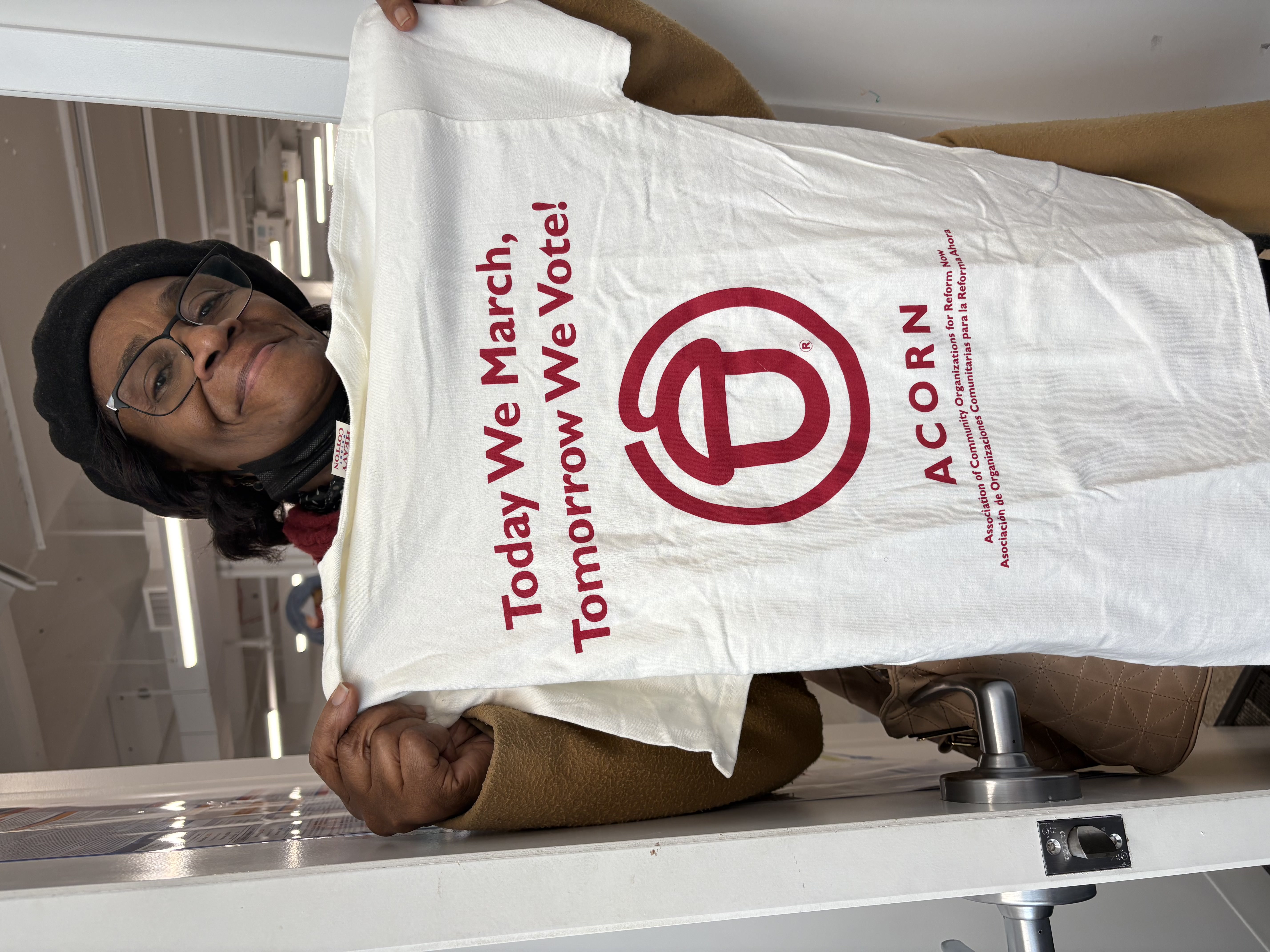 Member/leader Lucy Garroway holding up an ACORN T-shirt that says, “Today We March, Tomorrow We Vote!”