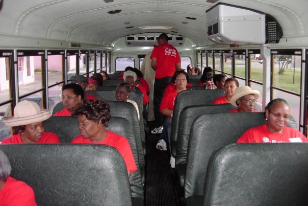 Photograph of ACORN members, all wearing red T-shirts that say, “Raise Wages!” on a school bus (photo credit: Tanya Harris-Glasow or Marie Hurt).
