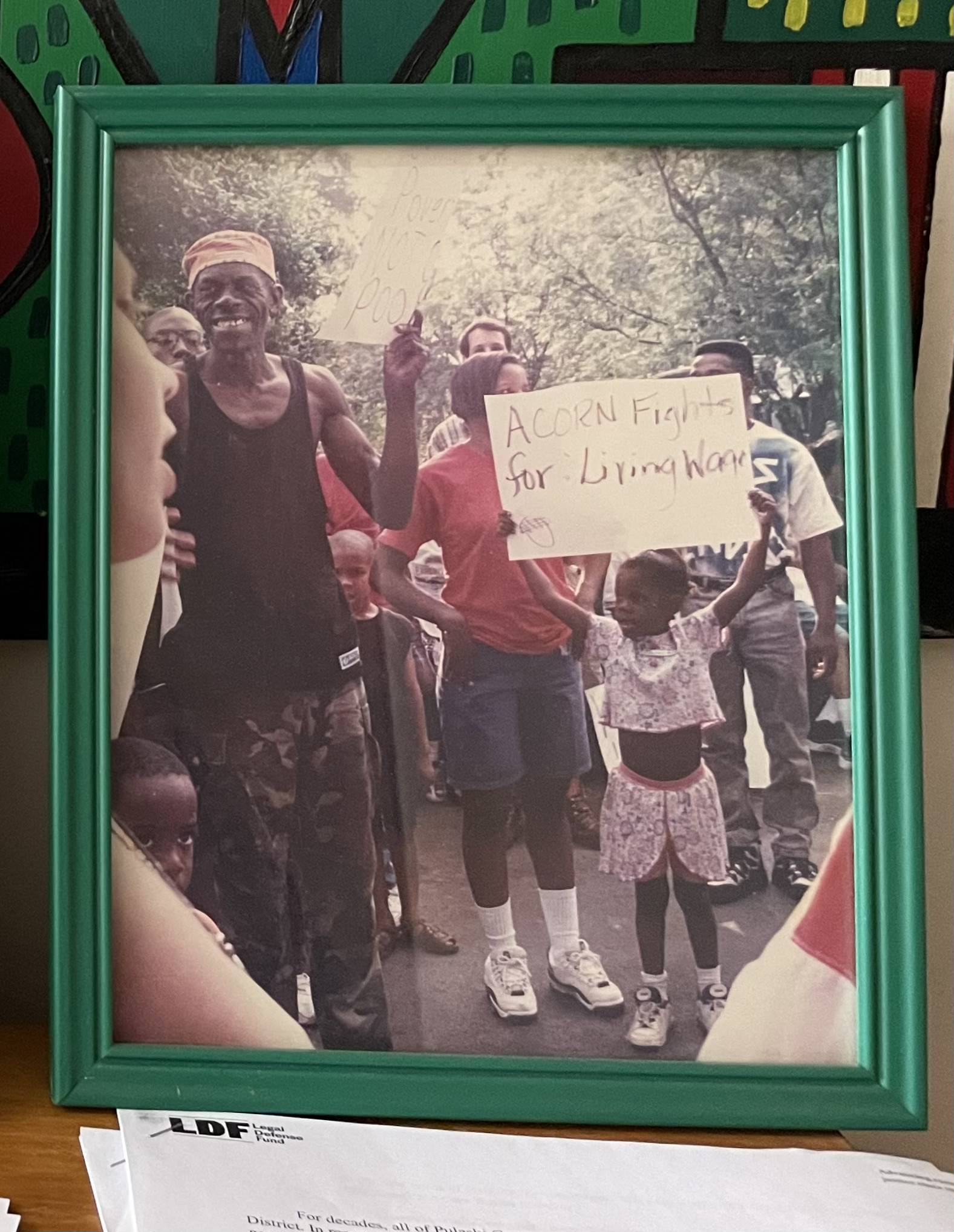 Framed photograph from the Arkansas Community Organizations (ACO) office in Little Rock, Arkansas, featuring a little girl holding up a sign that reads, “ACORN Fights for: Living Wage”